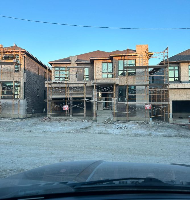 A large, multi-level house under construction with brick and stone siding, covered entirely by yellow metal scaffolding.